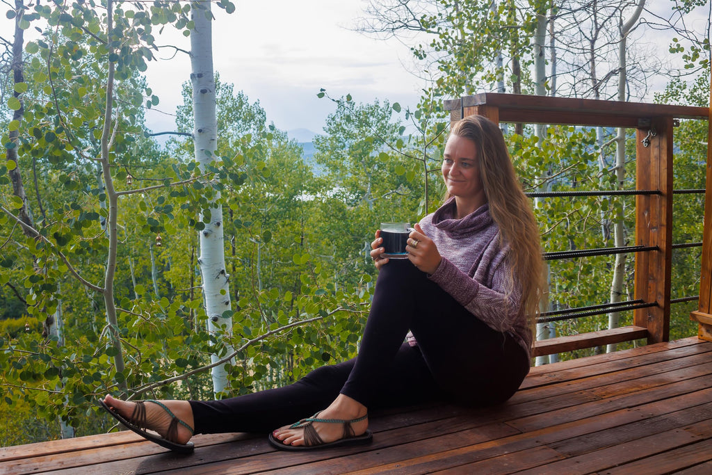 Woman sitting on a wooden deck holding a mug with trees in the background
