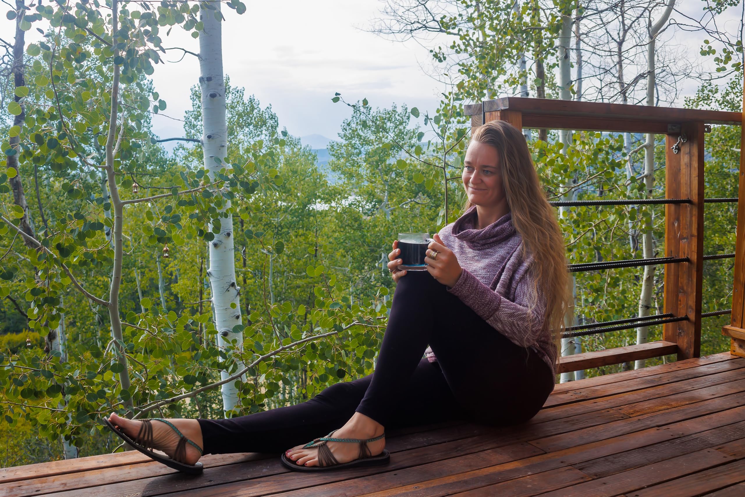 Woman sitting on a wooden deck holding a mug with trees in the background